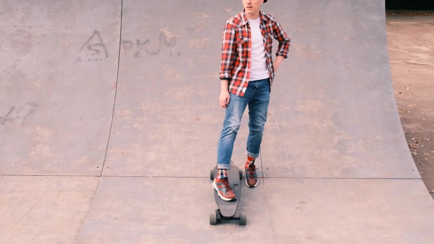Young male skateboarder standing on a ramp wearing jeans, plaid shirt and baseball cap, slow motion