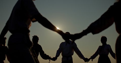 Close-up, people hold hands and lead a round dance, counterlight. Silhouettes of people in a round dance, against the light. 4k, ProRes
