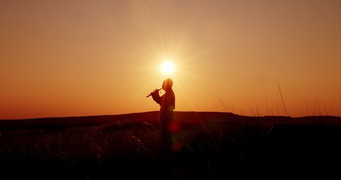 Sunset, silhouette of a man playing the pipe. Folk musician plays in the field, the culture of the peoples. 4k, ProRes