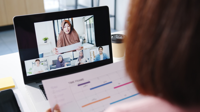 Young Asia businesswoman using laptop talk to colleague about plan in video call meeting while work from home at living room. Self-isolation, social distancing, quarantine for corona virus prevention. | Shutterstock HD Video #1064856772