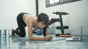 Young asian woman doing plank exercise and using laptop for digital workout sessions at home, Online training.