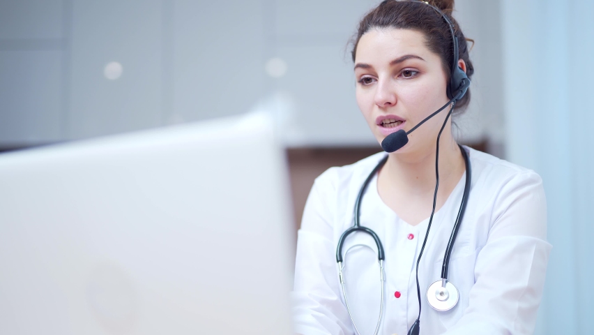 Medical online consultation, female doctor talking online with patient using laptop and headset. Call center office. Portrait of a woman specialist working remotely. Family doctor. Close up