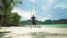 Man standing on wooden seat swinging hang on a tree on a tropical beach in resort at Phi Phi island, Krabi, Southern of Thailand in summer season, summer holiday and vacation
