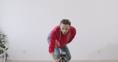 Young woman dancing and recording video with moves at camera in front of white wall background. Young woman having fun at home. Social media concept