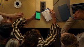 Top view of young woman sitting with green screen mobile phone at table near colleagues in office. Business people brainstorming in meeting room. Creative team working in coworking. - Powered by Shutterstock - Get 15% off with code: PIKWIZARD15