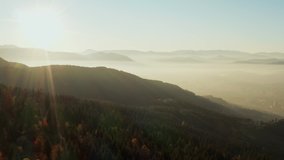 
Aerial view of the sun in the orange-golden sky that sets in the mountains that are shrouded in smoke and clouds in a landscape with peaks on which grow pine forests. Video of sunset and sunrise.