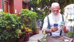 Senior hipster man holding coffee and having fun and looking in a modern phone on a europen city street, close up view, happiness, technology and elderly lifestyle people concept