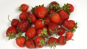 Closeup view video foootage of many riped red fresh organic strawberries on white background. Female and child's hands grabbing and eating berries.
