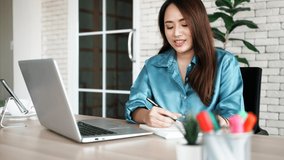 Authentic shot Businesswoman using laptop to work at office in her house happily. Asian freelance woman work hard with concentrated and smile happily, she succeed in job and has own business.