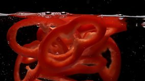 Red bell pepper slices falls down into clear water and floats up to surface edge on black background extreme closeup slow motion - Powered by Shutterstock - Get 15% off with code: PIKWIZARD15