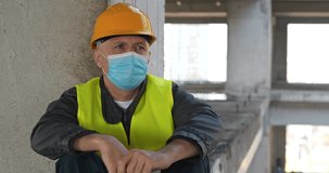 Worker in yellow hard hat and medical protective mask sits at construction site. He coughs and he is not feeling well. Cinema 4K 60fps video