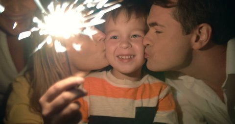 Happy family and Bengal fire at night. Mother holding sparkler, then she and father kissing child while he looking at light which going out at the end, videoclip de stoc