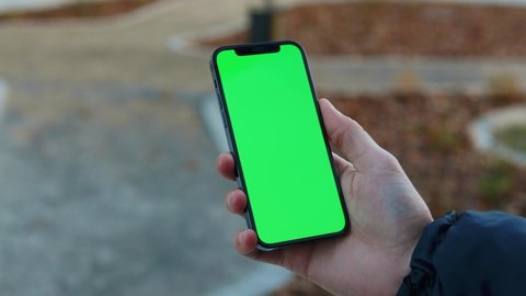 NEW YORK - December, 19 2020: Outdoors man hand using touch phone with vertical green screen background sunlight road in city blurred. Internet chrome outdoor cellular smartphone scrolling tapping