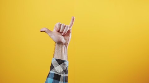 A male hand appears from below with a fist gesture and then makes a shaka gesture. Yellow background. The concept of gestures