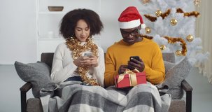 Couple do not speak to each other ignore feel offended boredom look at their mobile smartphones typing emails receive messages check mail go to social networks relaxing together on couch in new year