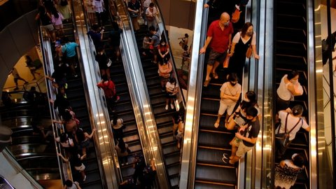 Singapore Dec 2020 Top down view of people with masks on the move on multi level escalators in crowded mall on weekend. Shopping mall is crowded with shoppers during end of year. Coronavirus outbreak