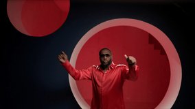 African American man dancing in the studio in a bright image. Portrait of a handsome guy dancing on a red background in a good mood. The expressive dancer moves effectively on the studio video. Slo-mo