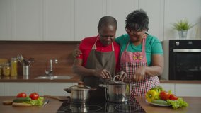 Happy surprised attractive retired african female in eyeglasses encouraging and supporting beloved black man cooking in domestic kitchen, tasting delicious meal and embracing husband with love. - Powered by Shutterstock - Get 15% off with code: PIKWIZARD15