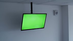 Man using remote control and watching TV with mock-up green screen at office or conference room. Change volume.