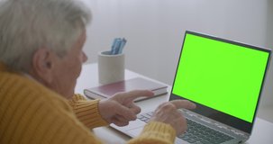 Mature woman nodding her head yes while looking at a green screen computer. Elderly mature woman with gray hair and a video call on her Laptop. Laptop with a green screen