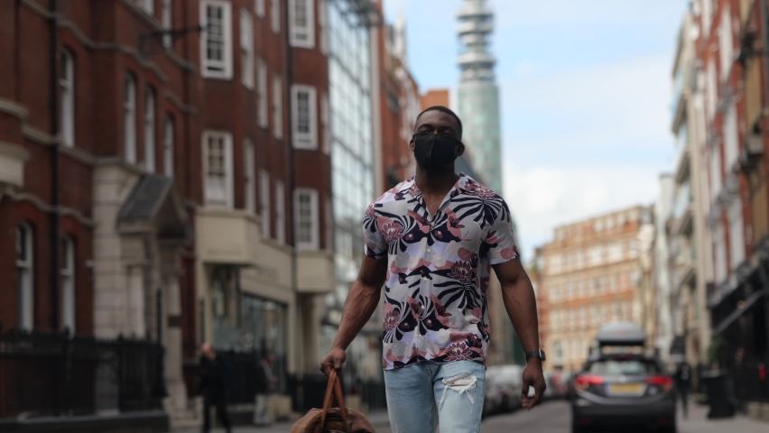 Black male wearing face mask walking under London skyline