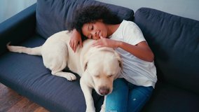 African american girl leaning and stroking dog while sitting on couch