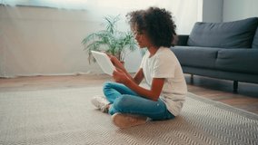 Side view of african american girl sitting on carpet and using digital tablet