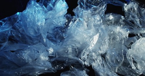 Used wet empty cellophane bags crushed plastic bottles trash waving on dark blue abstract water surface background.