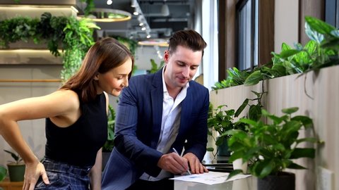 Caucasian businessman is signing agreement contract with his partner while working in green eco friendly modern working space surrounded by air purifying house plant
