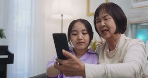 Asian grandmother and granddaughter video call at home. Happy senior and child using mobile phone video call talking with dad and mom sitting in living room at home.