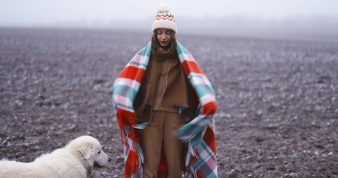 Portrait of a happy woman swinging a checkered plaid, having fun with a dog on the snowy field. Enjoying wintertime on nature. Slow motion