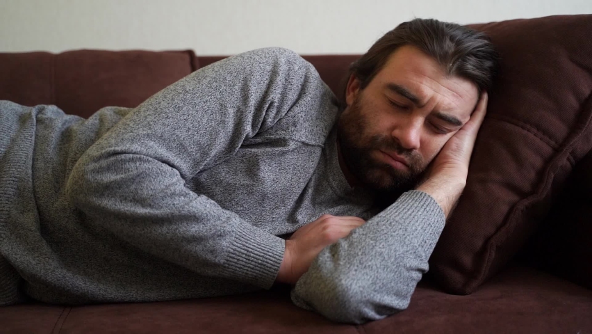 Guy sleeps on the sofa in the living room after party. Concept of after party, tired overworked person hard day, lack of energy, breakdown | Shutterstock HD Video #1064947219