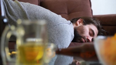 Drunk man falling on sofa.
Bearded male alcoholic falling on couch after drinking too much beer in weekend at home