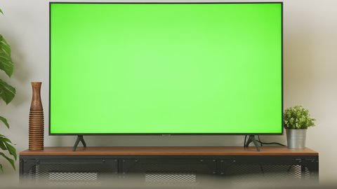 Zoom out shot of TV Green Screen in living room with tree and lamps. chroma key screen for advertising.