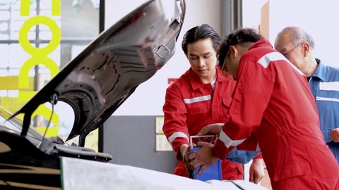 worker men and senior staff in factory dress repairing and checking battery a car engine a garage car parking. people working in industrial warehouse of spare parts transportation.