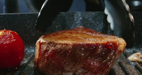 The chef flips a piece of grilling meat on grill pan