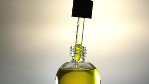 Cosmetic oil for skin and hair care, natural organic cosmetics, yellow oil dripping from pipette in glass bottle.