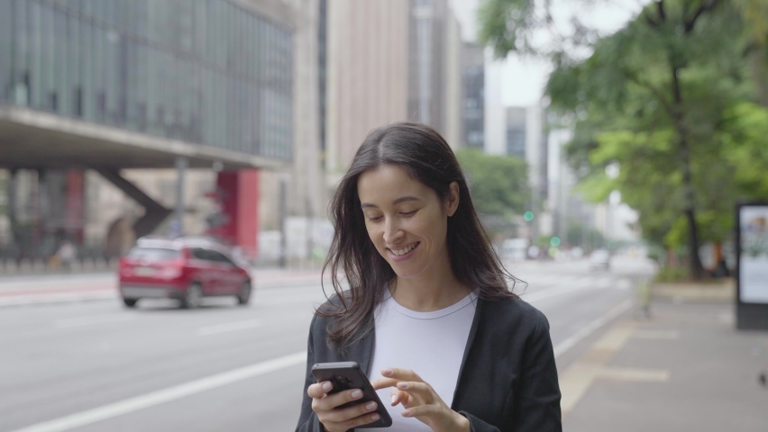 Smiling young woman walking around paulista avenue using smartphone. Communication, social networks, online shopping concept.
 Royalty-Free Stock Footage #1064960635