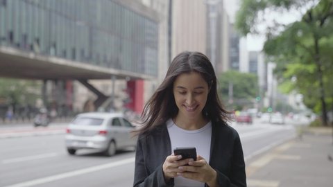 Smiling young woman walking around paulista avenue using smartphone. Communication, social networks, online shopping concept.
