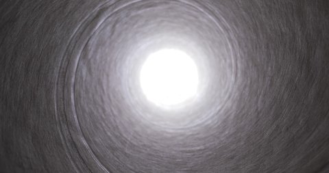Moving through a tube tunnel with bright light shining at the end, probe lens motion, falling into a well
