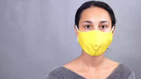 Young pretty mixed-race woman with yellow medical mask against gray background
