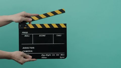 Movie Clapperboard. Film crew man hold and move up film slate in to the frame and clap it and move down out of the frame. yellow and black stripe  clapper board isolated on pastel blue background.