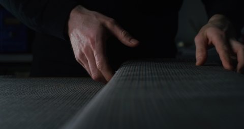 Cinematic macro shot of experienced tailor is controlling with hands fine quality fabric for creation custom haute couture apparel in tailoring workshop. Concept of handmade, couturier and tradition.