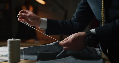 Cinematic shot of experienced tailor is sewing custom handmade high quality apparel in ancient luxury traditional tailoring workshop. Concept of industry, handmade, hand craft, couturier and tradition.