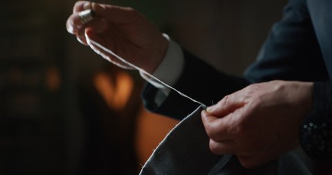 Cinematic shot of experienced tailor is sewing custom handmade high quality apparel in ancient luxury traditional tailoring workshop. Concept of industry, handmade, hand craft, couturier and tradition.