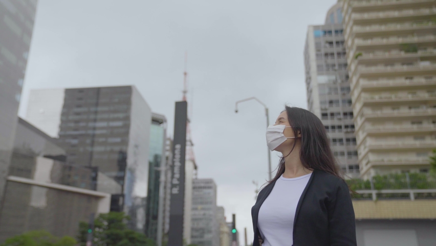 Confident Businesswoman wearing face mask look up big modern Business district. Woman looking up a sucessful life. 
