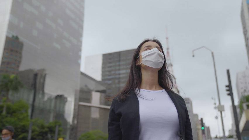 Confident Businesswoman wearing face mask look up big modern Business district. Woman looking up a sucessful life. 
