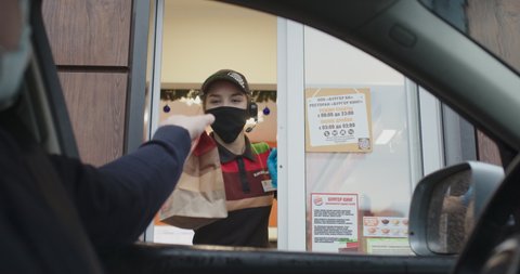 Worker in protective mask issues takeaway order at Burger King drive thru during a pandemic. Seller and buyer in medical masks for protection against viruses. Minsk, Belarus - December 28, 2020