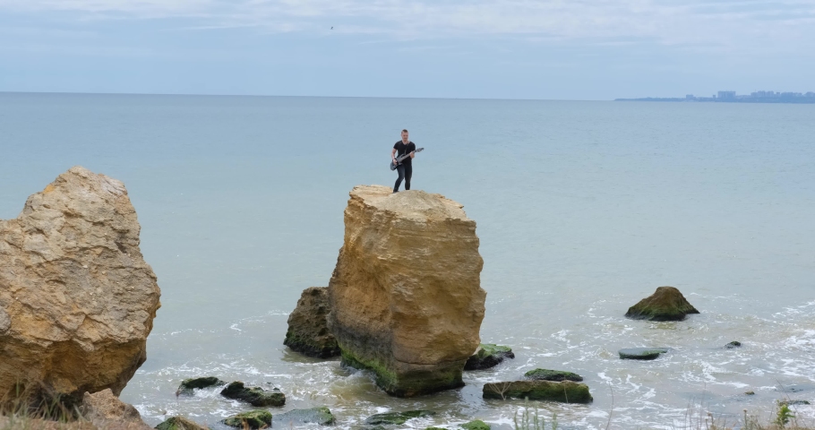 Male with electro guitar play outdoors on the beach 