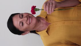 An old woman on a white background holding a red rose in her hand. The woman smells the rose.Video for the vertical story.
